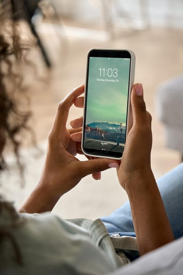 Young African American woman hands holding cell phone with mockup white blank display, empty screen for app ads at home. Mobile applications technology concept, over shoulder close up view.